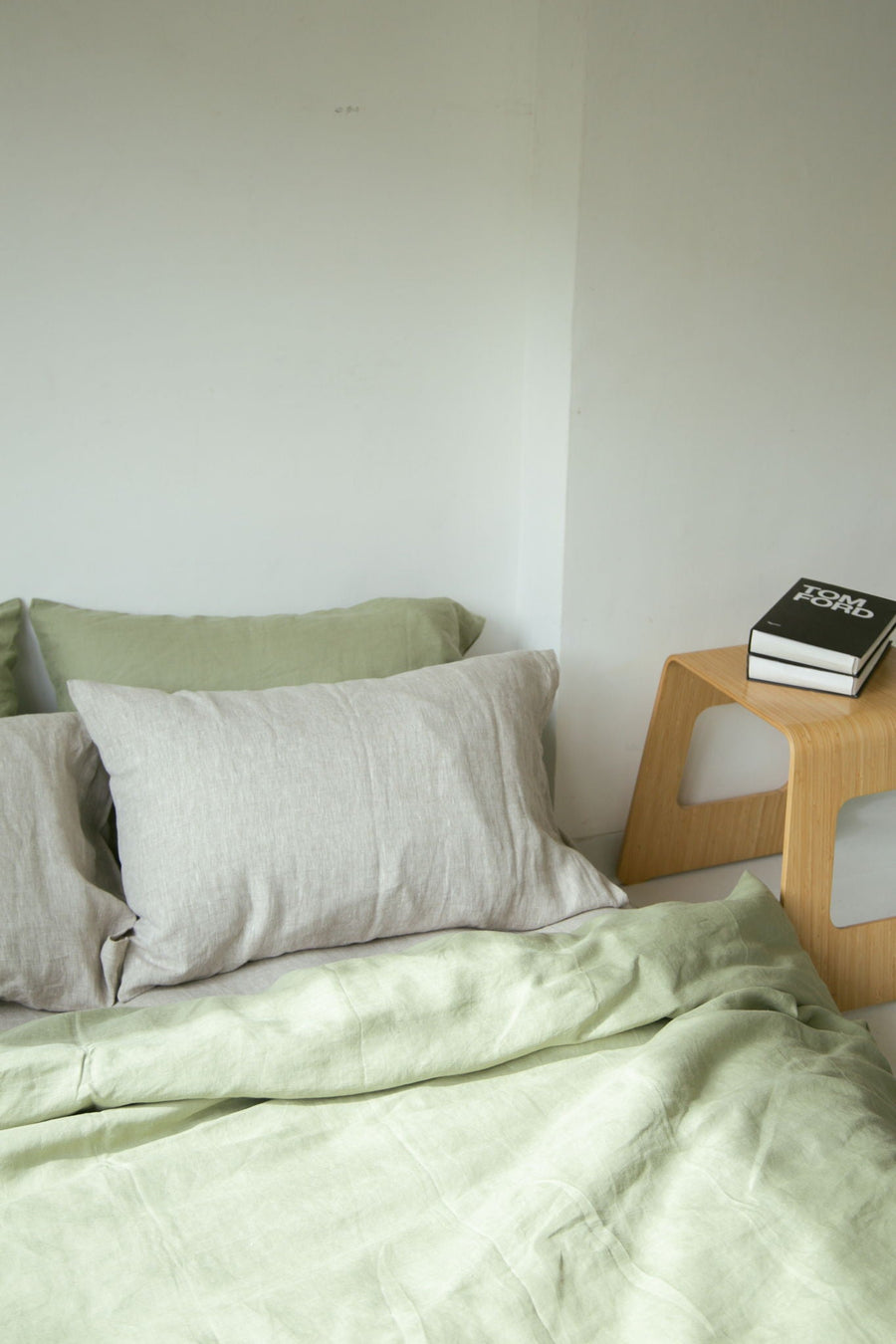 Sage French flax linen bedding on a made bed with a wooden side table, The Katha