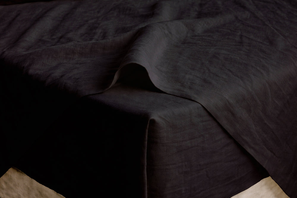 Black French linen sheet draped over a mattress corner, close-up