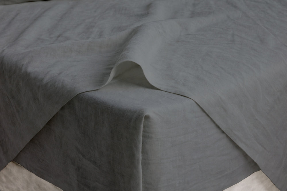 Smoke grey French linen sheet draped over a mattress corner, close-up