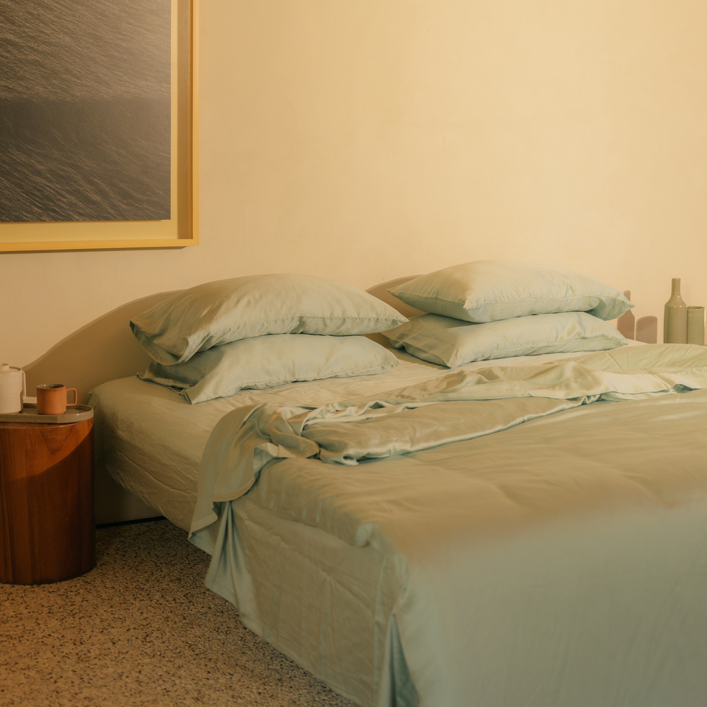 Mint green eucalyptus TENCEL bundle set on a bed below a framed sea photograph