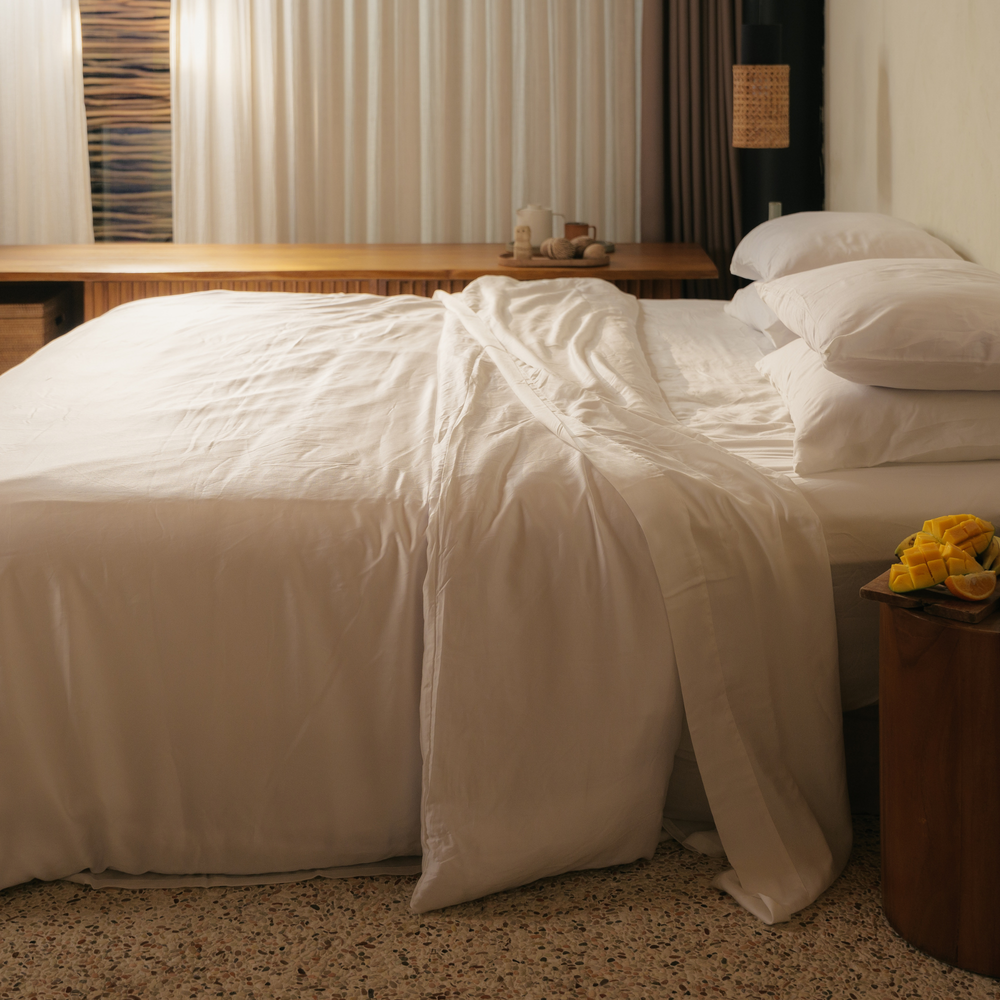 White eucalyptus TENCEL bundle set draped off a bed by a curtained window