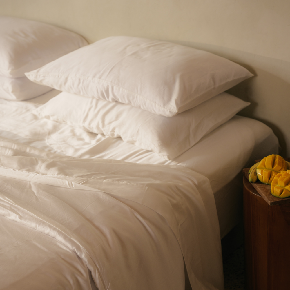 White eucalyptus TENCEL pillows stacked on a made bed beside yellow flowers