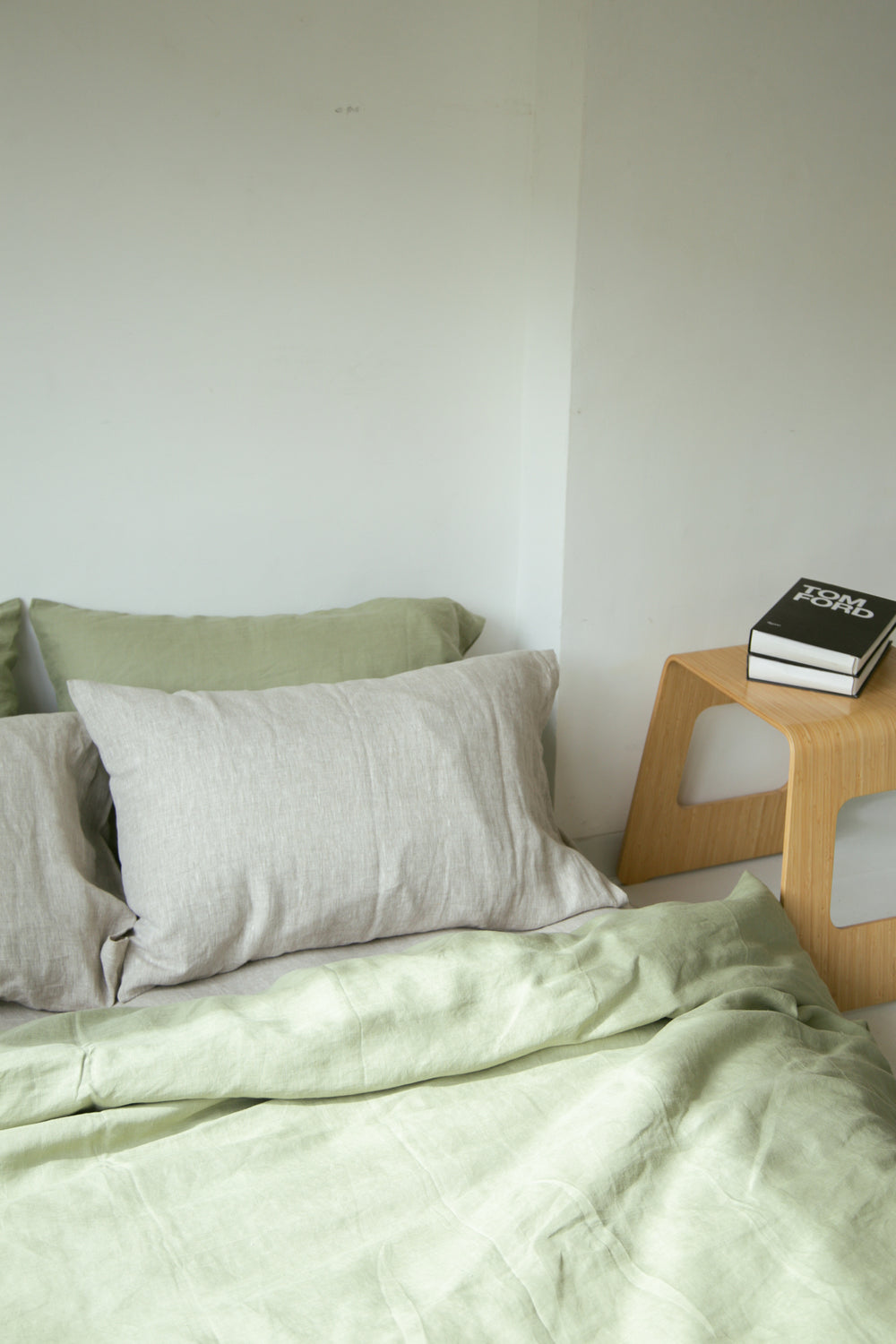 Sage green French linen duvet cover with grey pillowcases beside a wooden side table